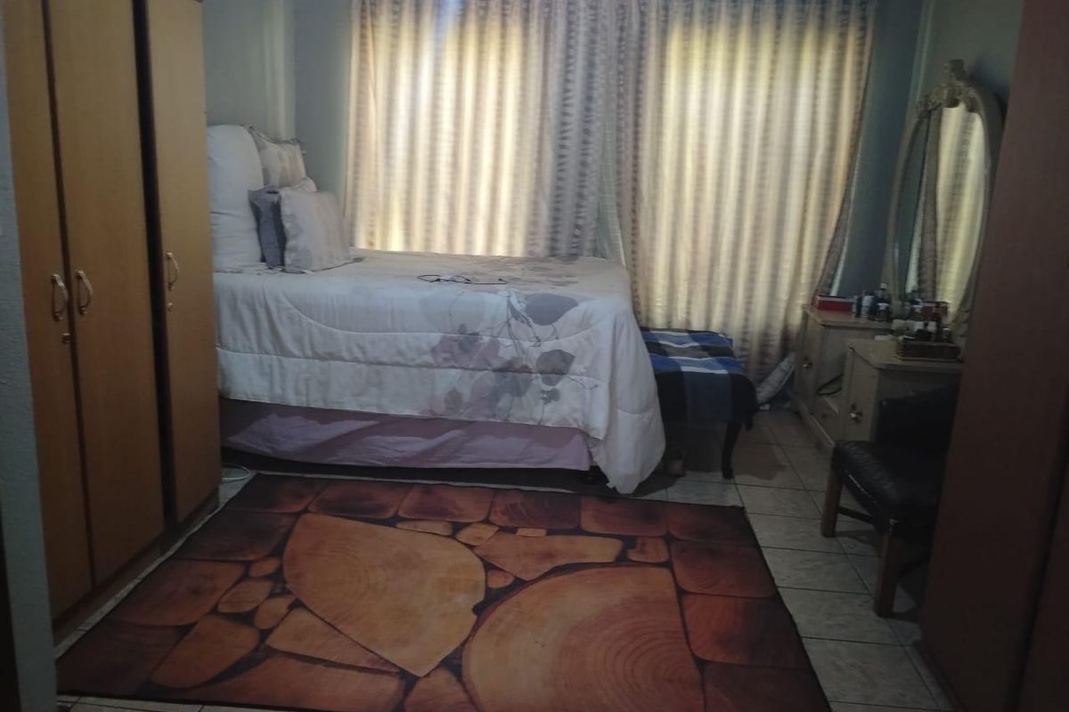 A bedroom featuring tiled flooring and built-in cabinetry, offering a functional space with natural light filtered through window curtains.