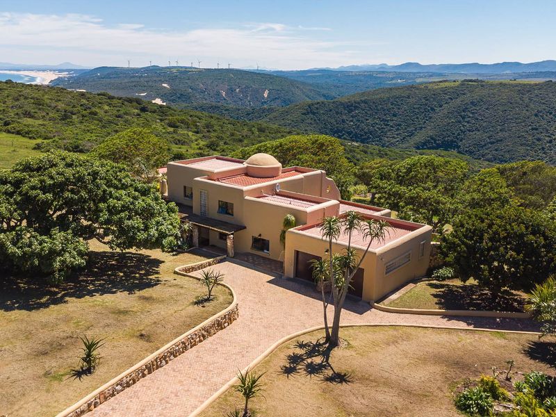 Aerial view of a Mediterranean-style small holding featuring a paved driveway, stone retaining walls, and expansive surrounding landscape with distant coastal views.