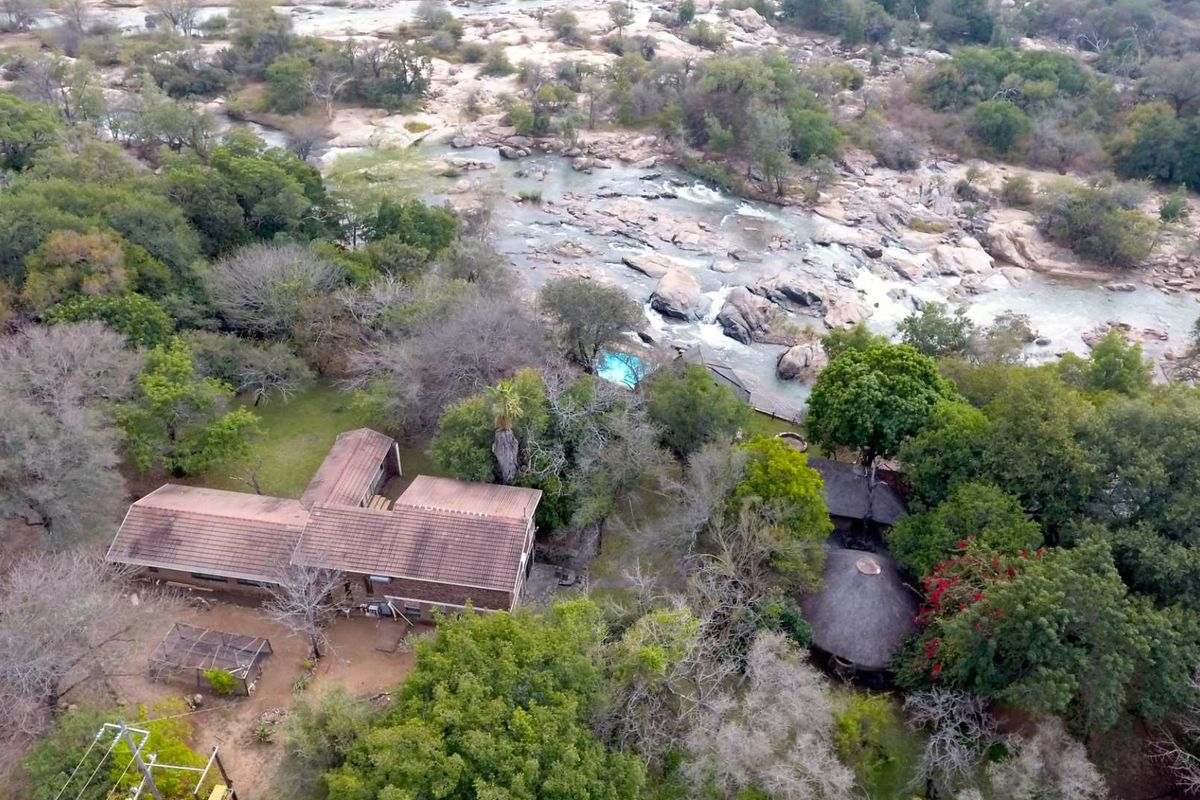 Aerial view of a property featuring multiple structures, a swimming pool, and extensive natural river frontage within a wooded landscape.