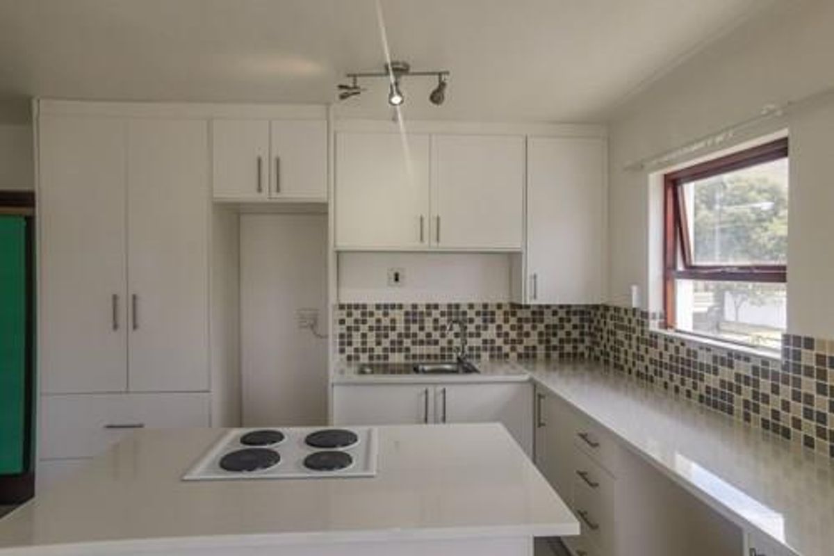 A clean, modern kitchen featuring white cabinetry, quartz countertops, a built-in electric hob, and a decorative mosaic tile backsplash.