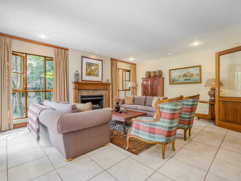 Spacious living room featuring a stone fireplace, tiled flooring, and large timber-framed windows providing natural light and garden views.