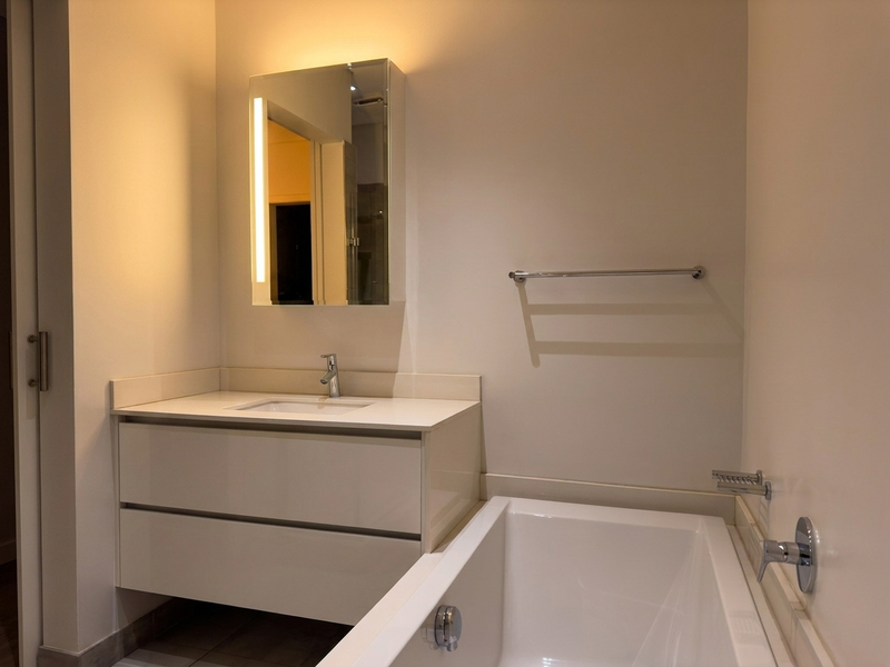 Modern bathroom featuring a sleek vanity with integrated basin, mirrored medicine cabinet with LED lighting, and a clean white bathtub.