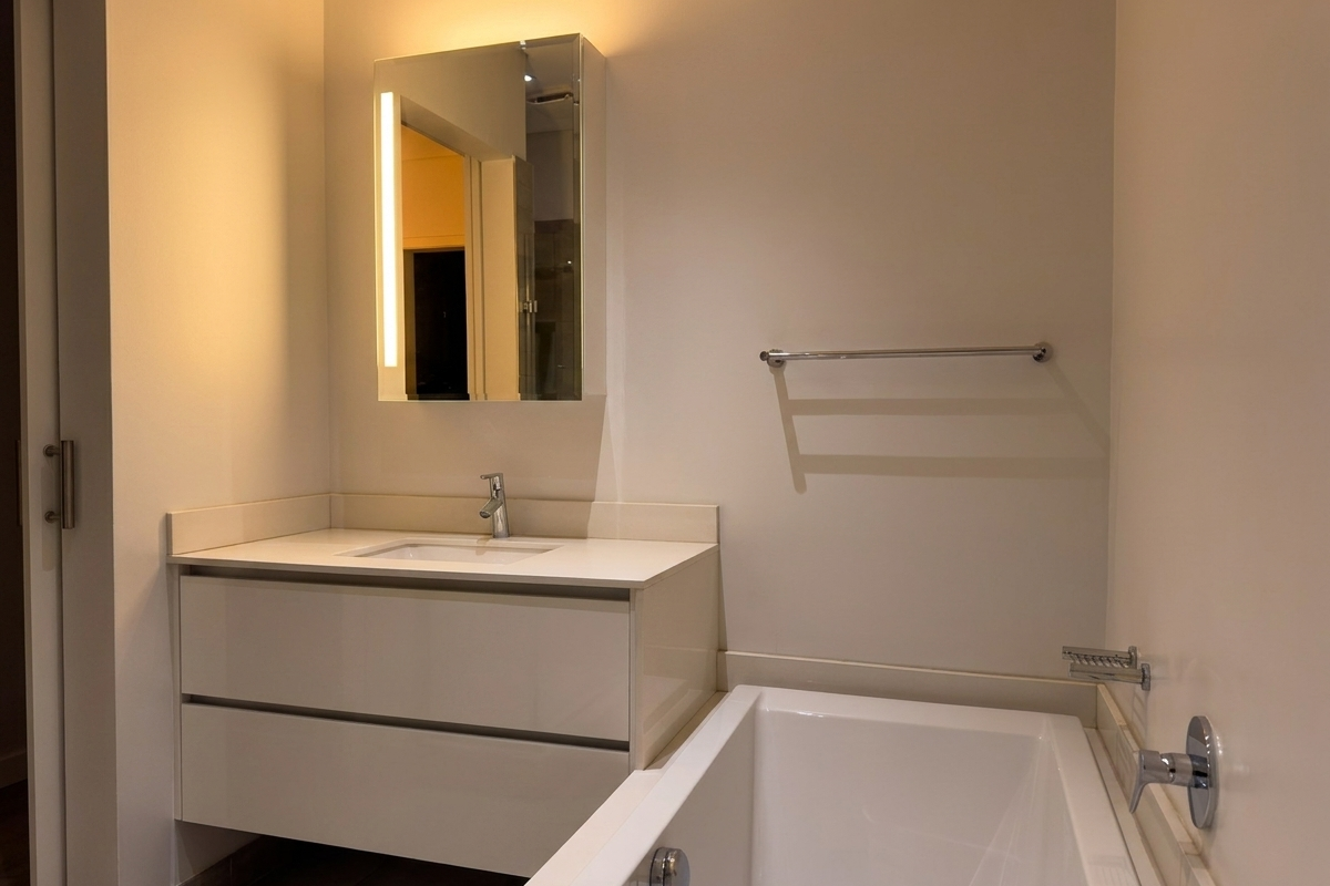 Modern bathroom featuring a sleek vanity with integrated basin, mirrored medicine cabinet with LED lighting, and a clean white bathtub.