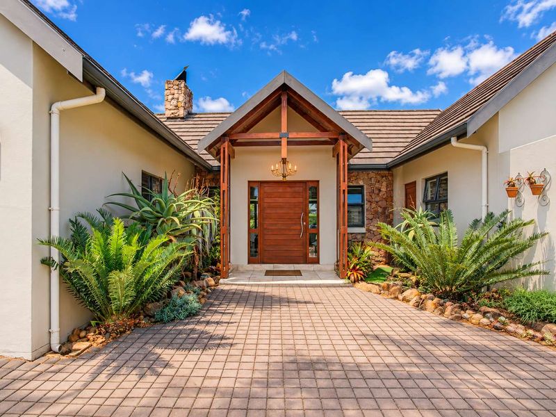 A well-maintained front entrance featuring a timber door, stone cladding accents, and a paved driveway leading to a covered portico.