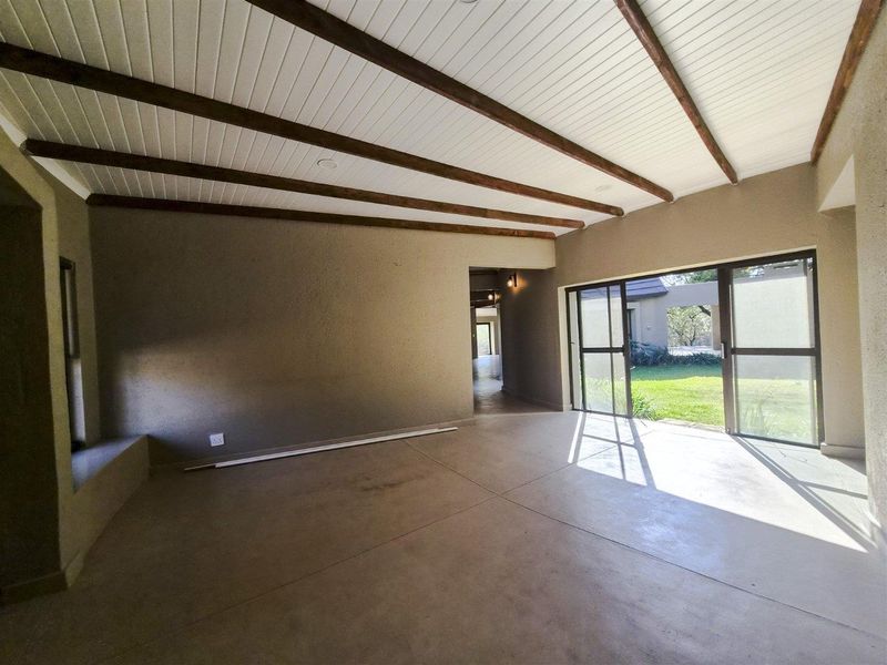 Spacious covered patio featuring exposed timber ceiling beams, concrete flooring, and large sliding glass doors opening to the garden.