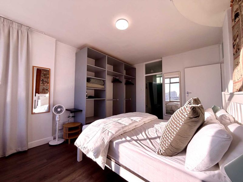 A well-lit bedroom featuring dark laminate flooring and a large, open-concept built-in wardrobe with ample storage space.