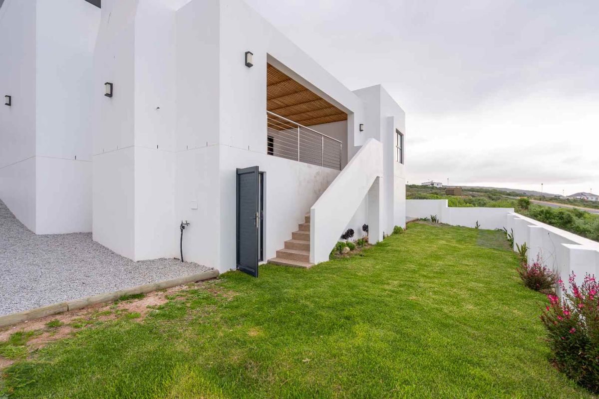 A modern exterior view of the rear of the house, featuring a white facade, an elevated patio with a wooden pergola, and a landscaped lawn.