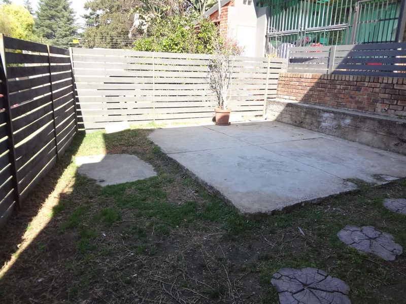 A private rear courtyard area featuring a concrete patio slab, timber slat fencing, and a brick retaining wall, offering potential for outdoor landscaping.