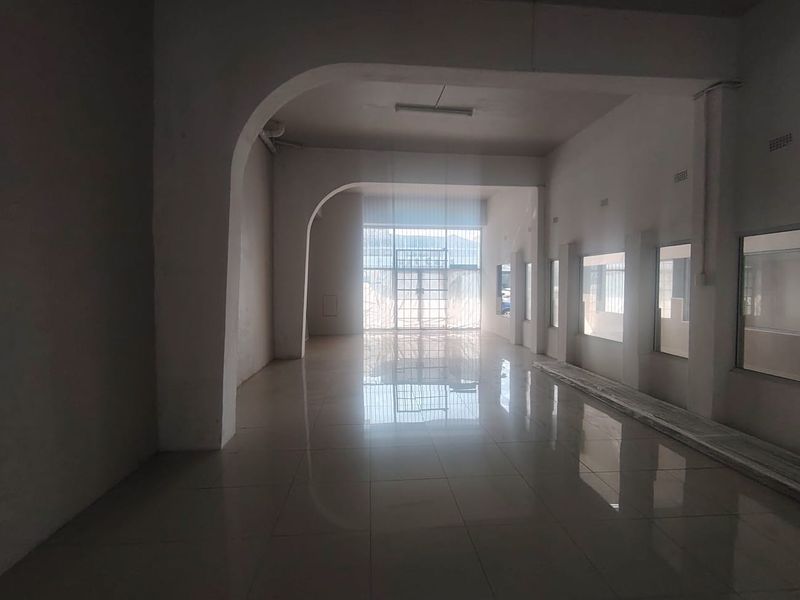 A spacious, empty open-plan commercial or retail area featuring tiled floors, arched architectural details, and large windows providing natural light.