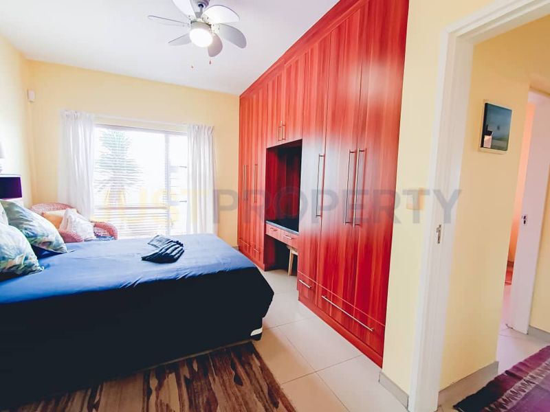 A bedroom featuring extensive built-in wooden cabinetry, tiled flooring, and a ceiling fan, offering functional storage and a neutral layout.