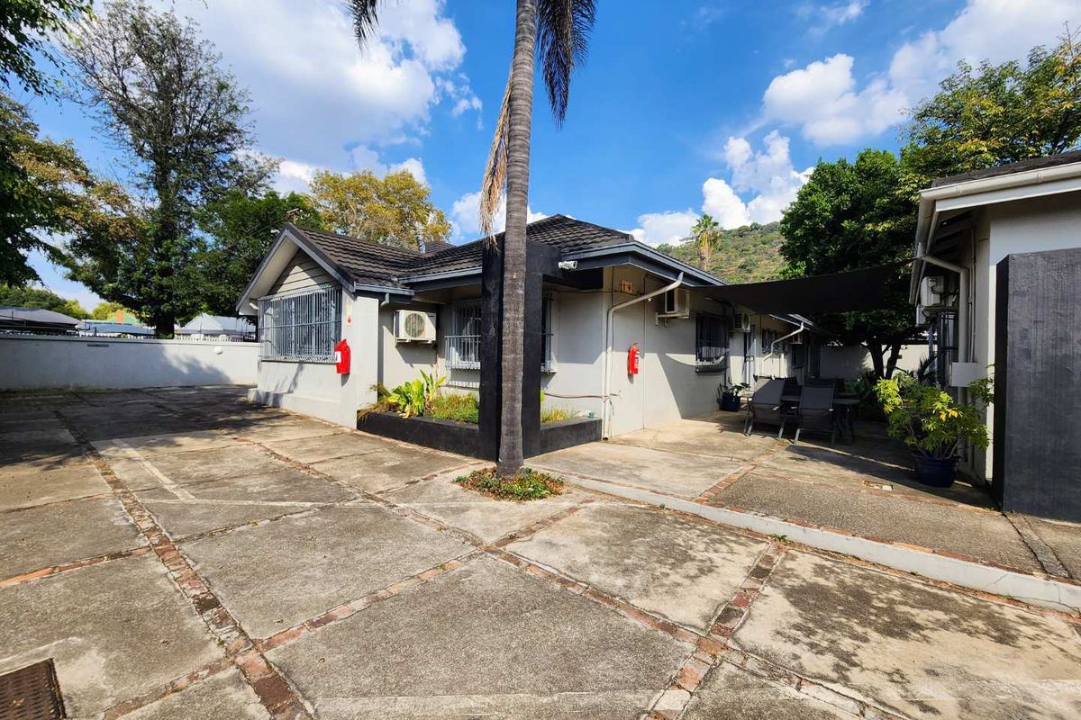 Exterior view of the property featuring a paved driveway, covered patio area, and established garden surroundings with mounted air conditioning units.