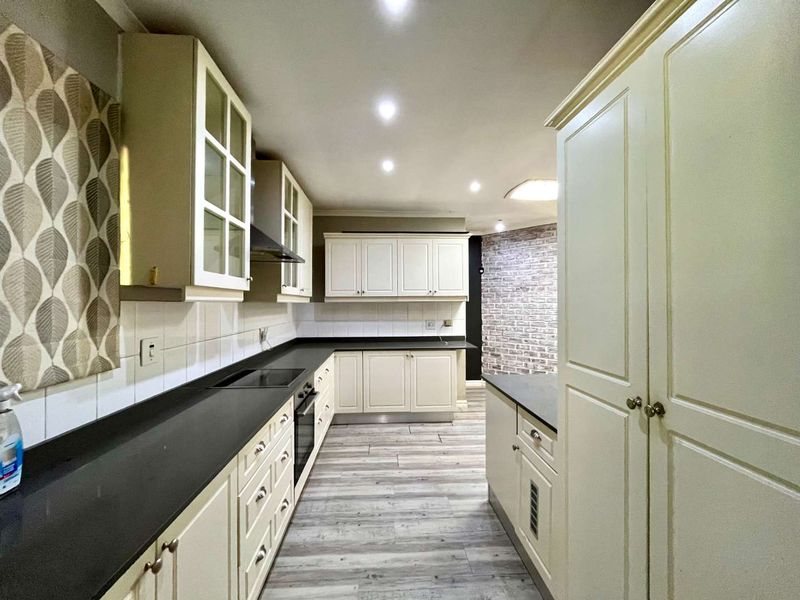 A clean, well-lit kitchen featuring ample built-in cabinetry, dark laminate countertops, integrated appliances, and modern wood-look laminate flooring.