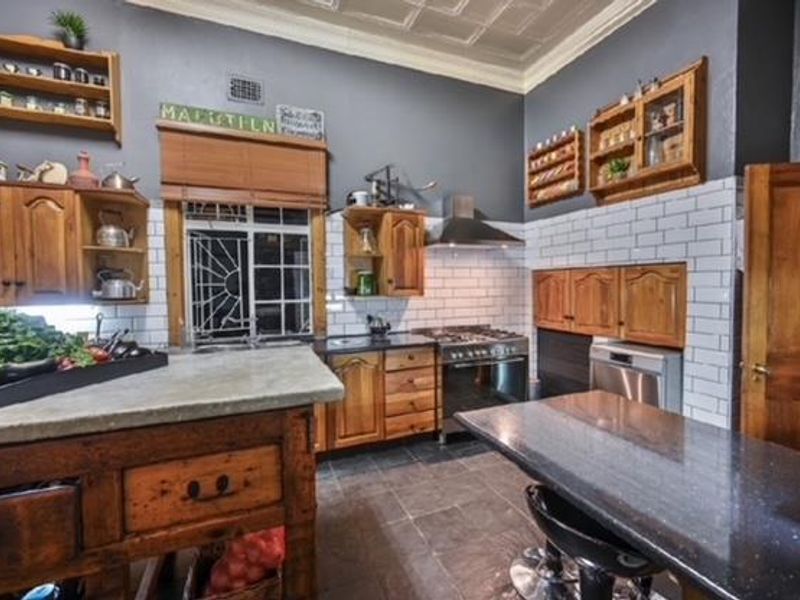 A rustic-style kitchen featuring wooden cabinetry, subway tile backsplash, stone countertops, a gas stove, and a distinctive pressed metal ceiling.