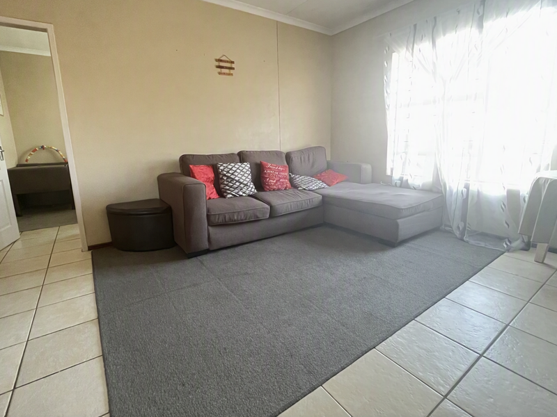 A living room featuring tiled flooring and a large window with security bars, providing access to an adjacent room.