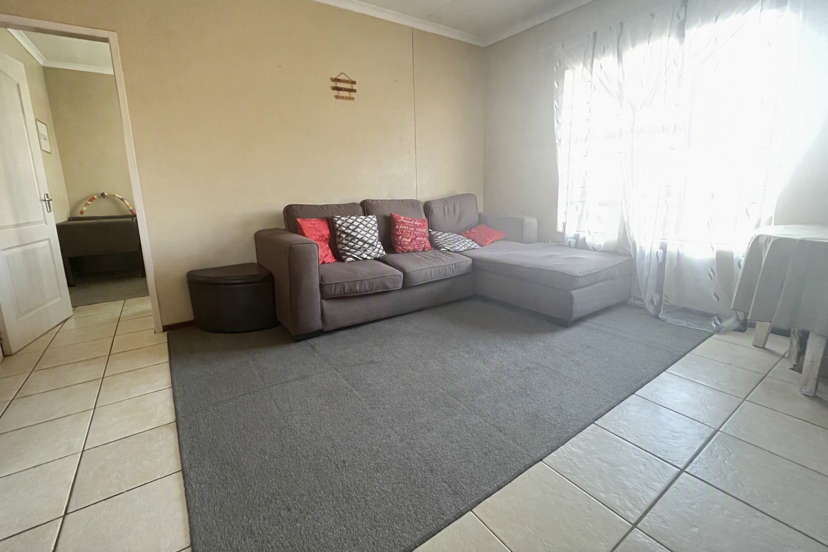A living room featuring tiled flooring and a large window with security bars, providing access to an adjacent room.