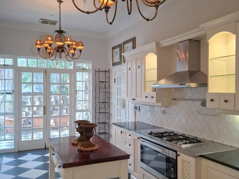 A well-appointed kitchen featuring classic cabinetry, stone countertops, a gas cooktop, and elegant chandeliers, with direct access to the outdoor area through french doors.