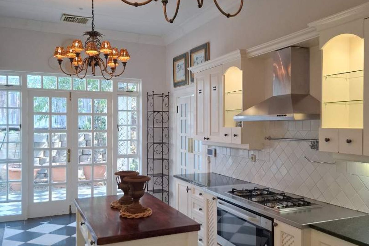 A well-appointed kitchen featuring classic cabinetry, stone countertops, a gas cooktop, and elegant chandeliers, with direct access to the outdoor area through french doors.