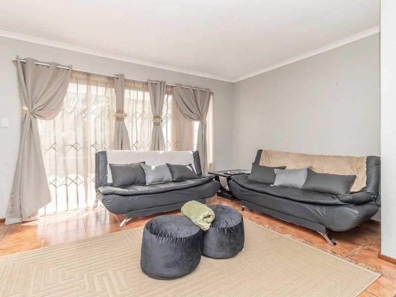 A bright living room featuring tiled flooring and a sliding glass door with an integrated security gate, providing access to the outdoor area.