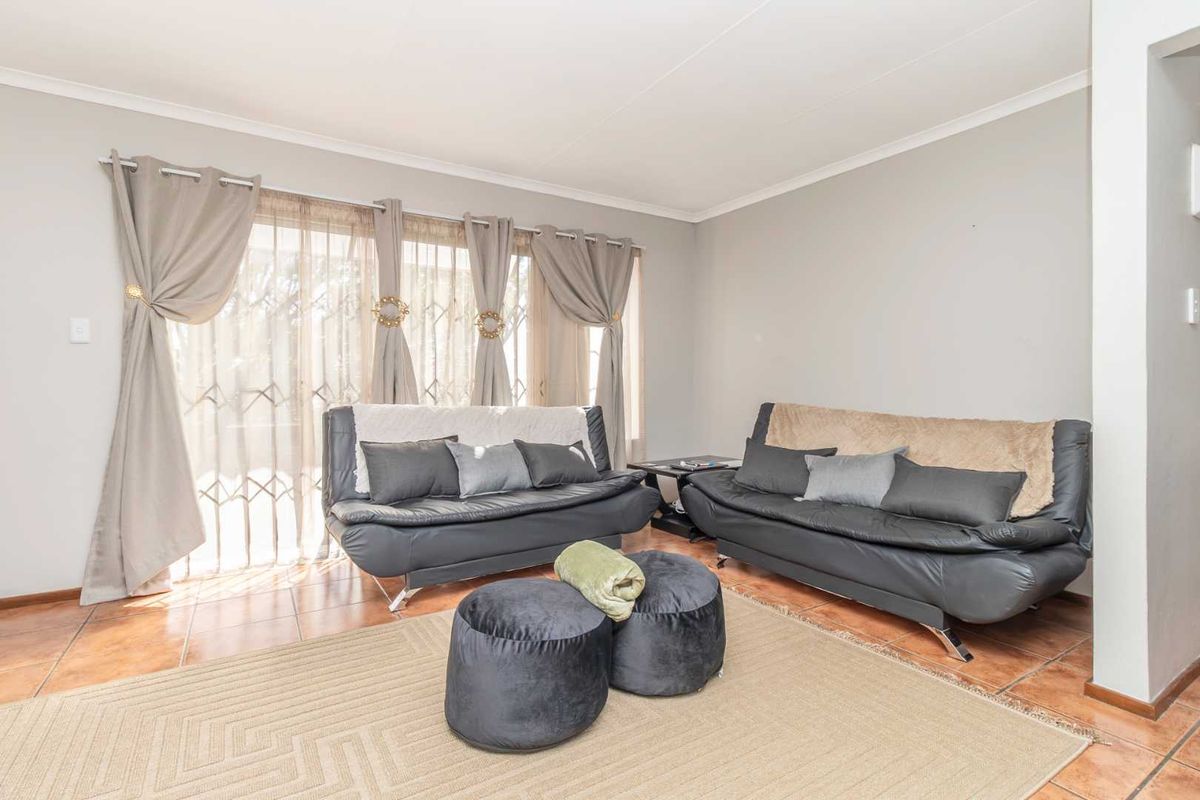 A bright living room featuring tiled flooring and a sliding glass door with an integrated security gate, providing access to the outdoor area.