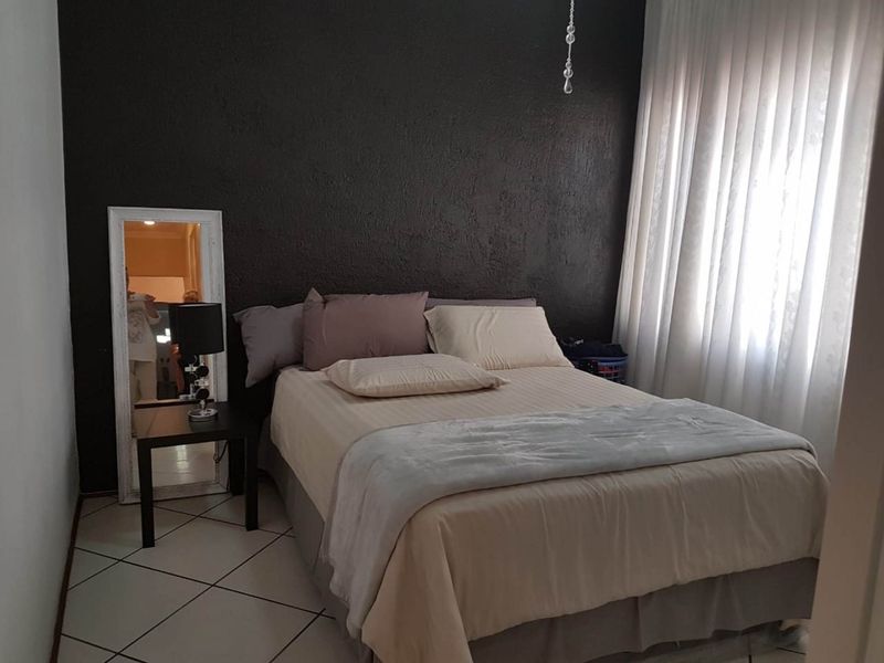 A bedroom featuring a dark textured accent wall, tiled flooring, and large window with curtains.