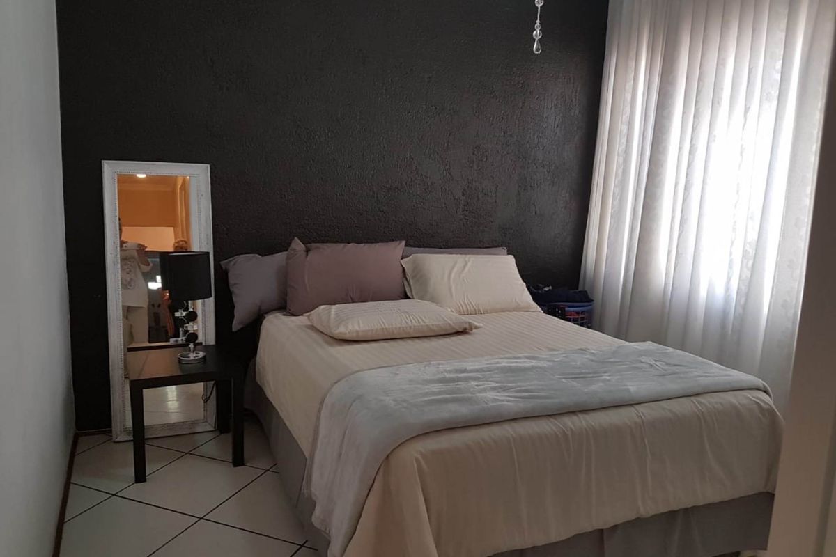 A bedroom featuring a dark textured accent wall, tiled flooring, and large window with curtains.