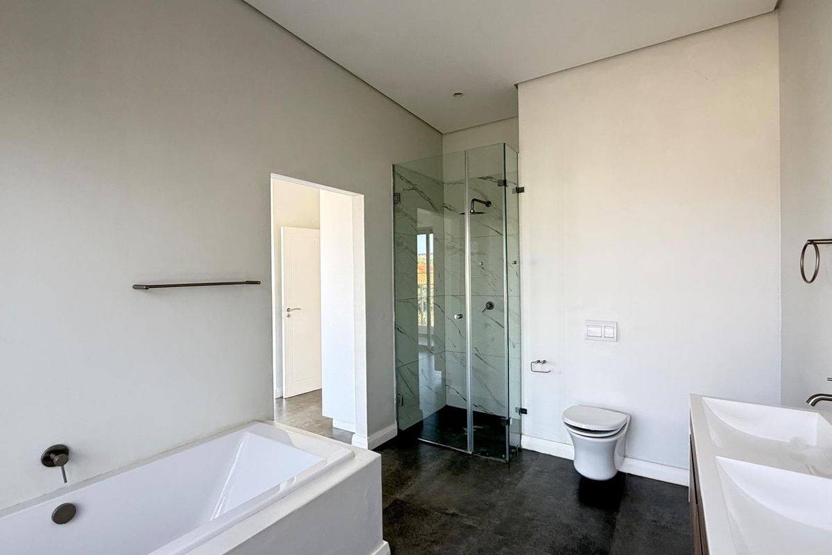 Modern bathroom featuring a built-in bathtub, glass-enclosed shower, wall-mounted toilet, and a double vanity with contemporary fixtures.