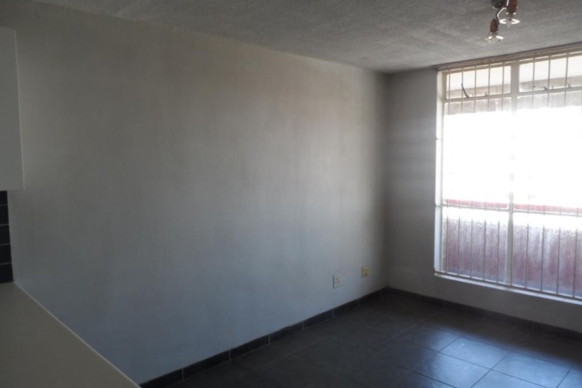 An empty living area featuring dark tiled flooring, a large window with security bars, and a simple ceiling light fixture.