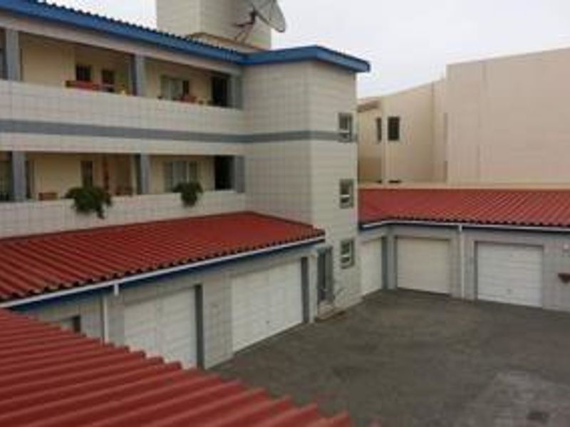 Rear view of an apartment complex featuring multiple garage units, tiled roofing, and upper-level balconies.