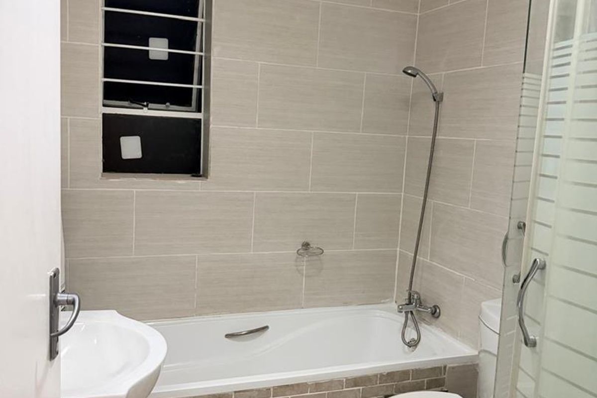 A clean, modern bathroom featuring a bathtub, separate shower enclosure, pedestal basin, and neutral wall tiling.