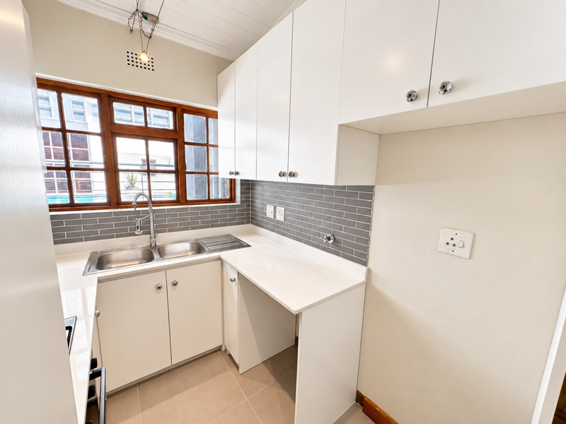 A clean, modern kitchen featuring white cabinetry, quartz countertops, a stainless steel double sink, and a stylish grey subway tile backsplash.