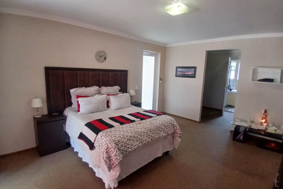 Spacious bedroom featuring neutral wall tones, carpeted flooring, and a built-in headboard, with direct access to an adjoining ensuite bathroom.