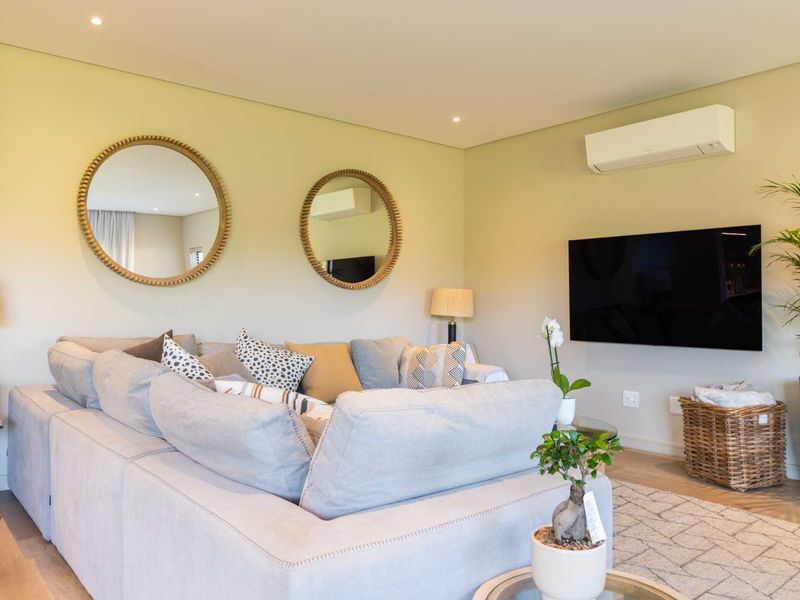 A well-maintained living room featuring recessed downlighting, laminate flooring, and a wall-mounted air conditioning unit.