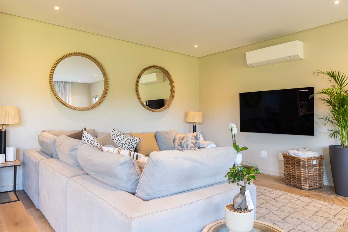 A well-maintained living room featuring recessed downlighting, laminate flooring, and a wall-mounted air conditioning unit.
