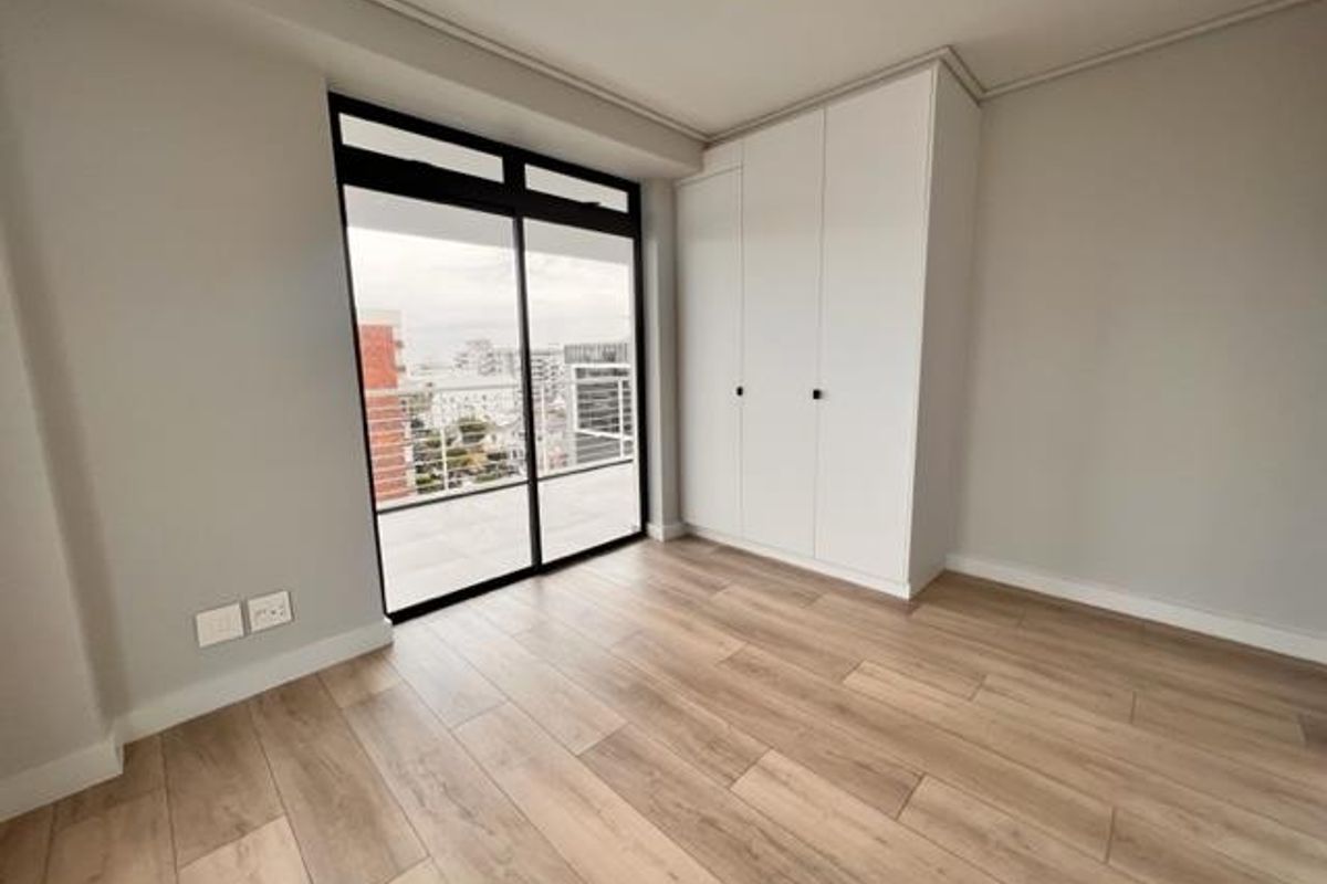 A bright, modern bedroom featuring wood-look tile flooring, a built-in wardrobe, and a sliding glass door leading to an outdoor balcony.