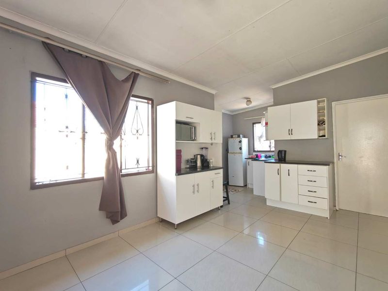 A functional kitchen featuring white built-in cabinetry, laminate countertops, and tiled flooring, with natural light provided by a window with security bars.