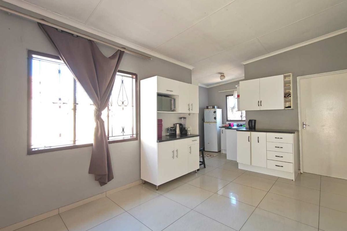 A functional kitchen featuring white built-in cabinetry, laminate countertops, and tiled flooring, with natural light provided by a window with security bars.