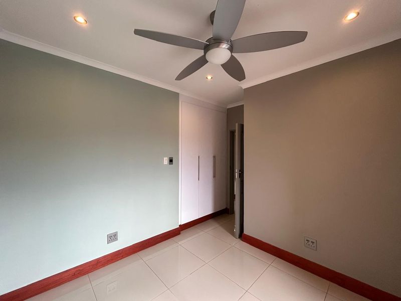 A clean, empty bedroom featuring neutral-toned walls, built-in cupboards, tiled flooring, and a modern ceiling fan with recessed lighting.