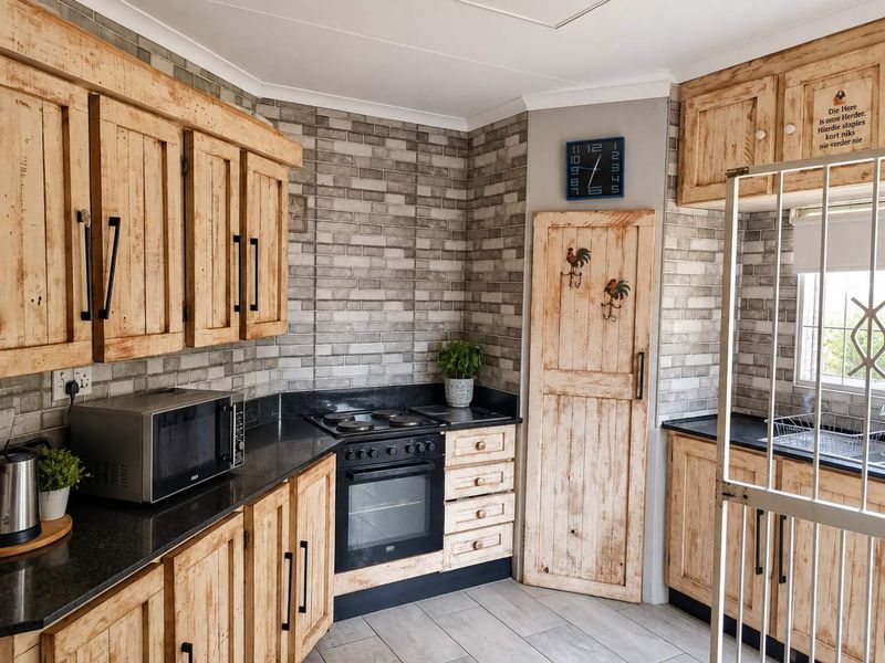 A rustic-style kitchen featuring wooden cabinetry, black granite countertops, a built-in oven and hob, and a decorative brick-style tiled backsplash.