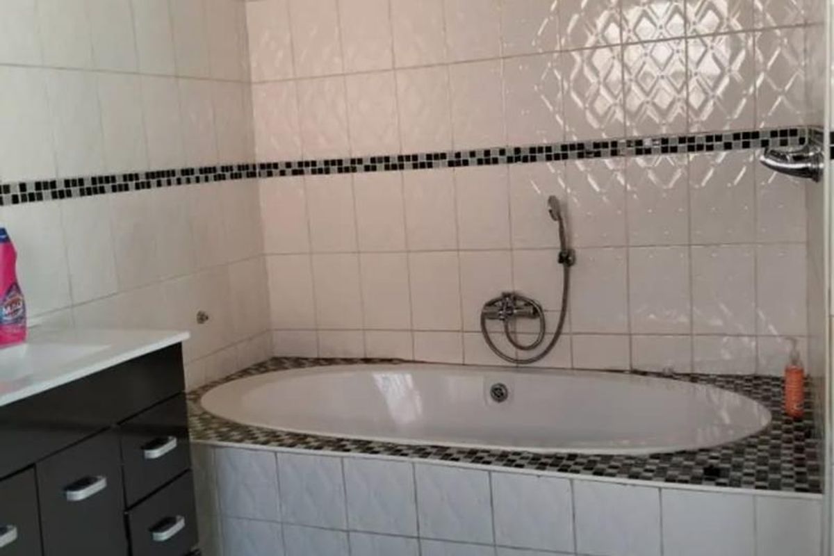 A functional bathroom featuring a built-in bathtub with a handheld shower mixer and a dark-toned vanity cabinet with integrated sink.