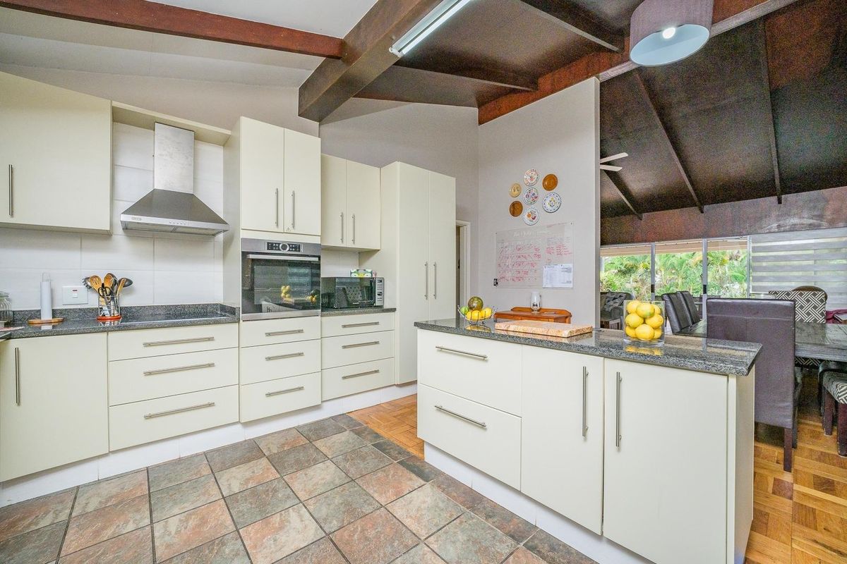 A well-maintained kitchen featuring cream cabinetry, granite countertops, a central island, and exposed timber beams, seamlessly flowing into the adjacent dining area.