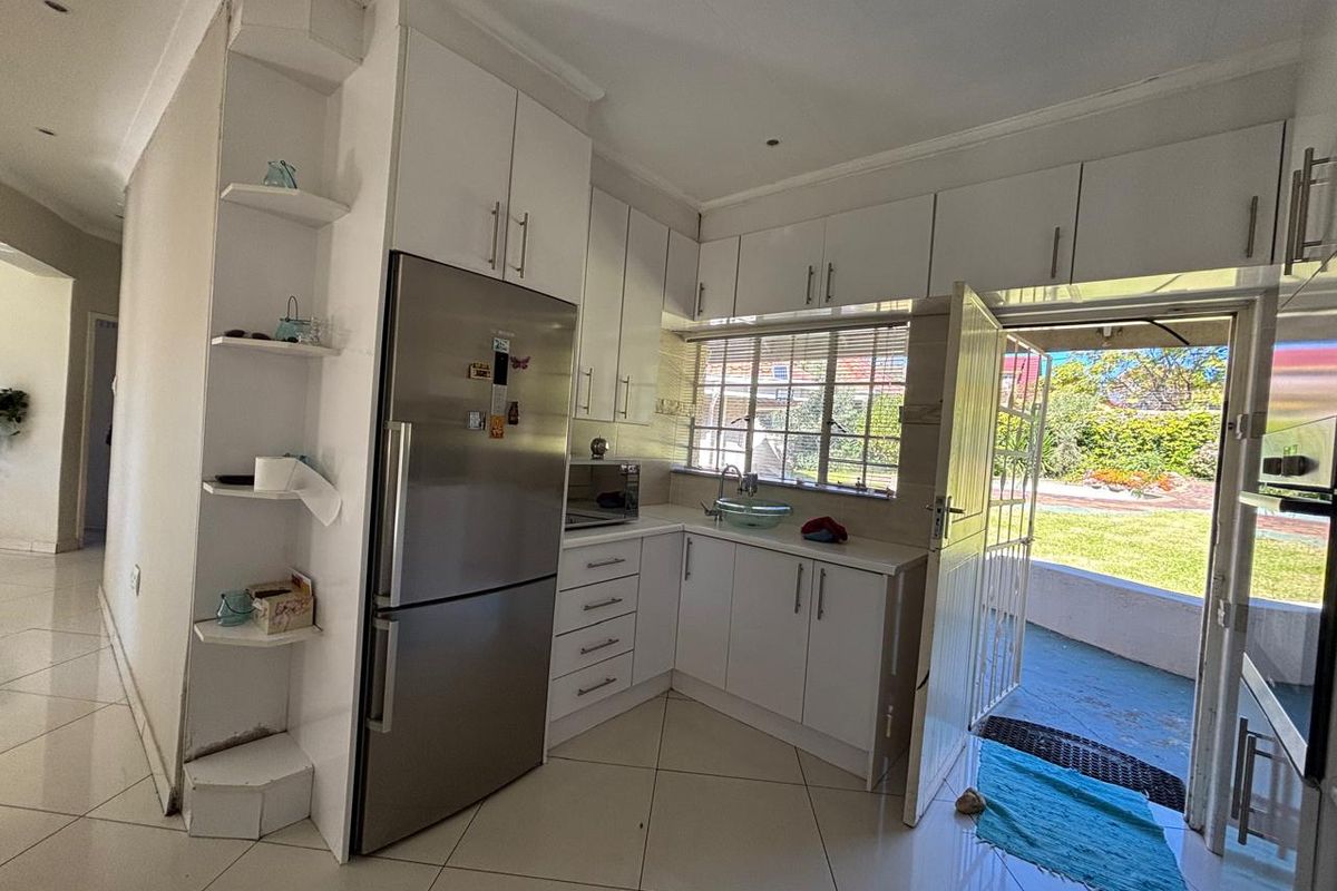 Compact kitchen featuring white cabinetry, stainless steel refrigerator, and direct access to the rear garden through a security gate.
