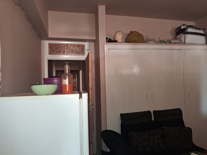 A bedroom featuring built-in cupboards and a ceiling bulkhead, requiring cosmetic updates to the door frames and wall finishes.