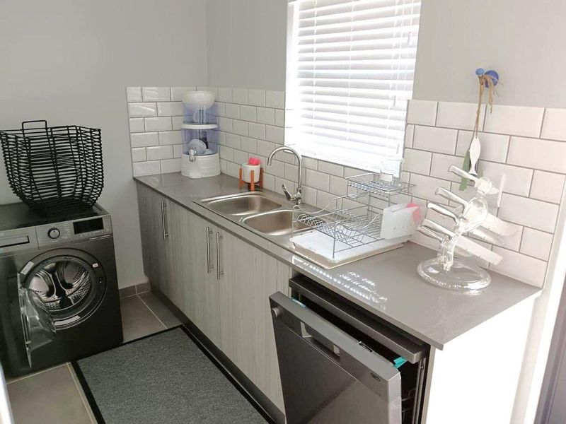 A functional laundry room featuring modern cabinetry, stone countertops, a double sink, and a subway tile backsplash with integrated appliance space.