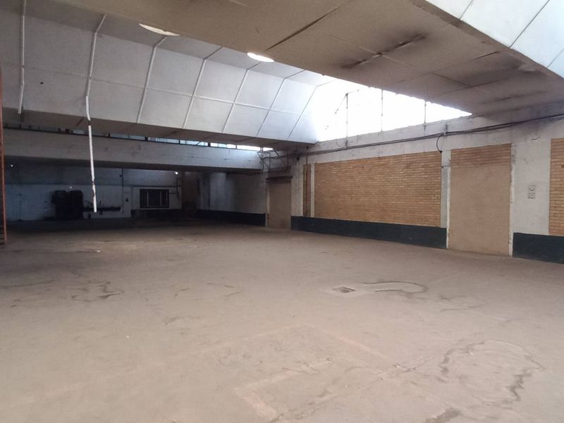 Spacious industrial warehouse area featuring high ceilings, exposed brickwork, concrete flooring, and a mezzanine access staircase.
