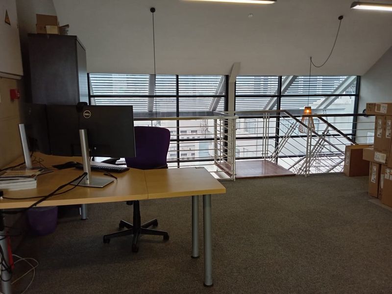 Open-plan office mezzanine area featuring large windows, carpeted flooring, and a metal staircase railing overlooking the lower level.