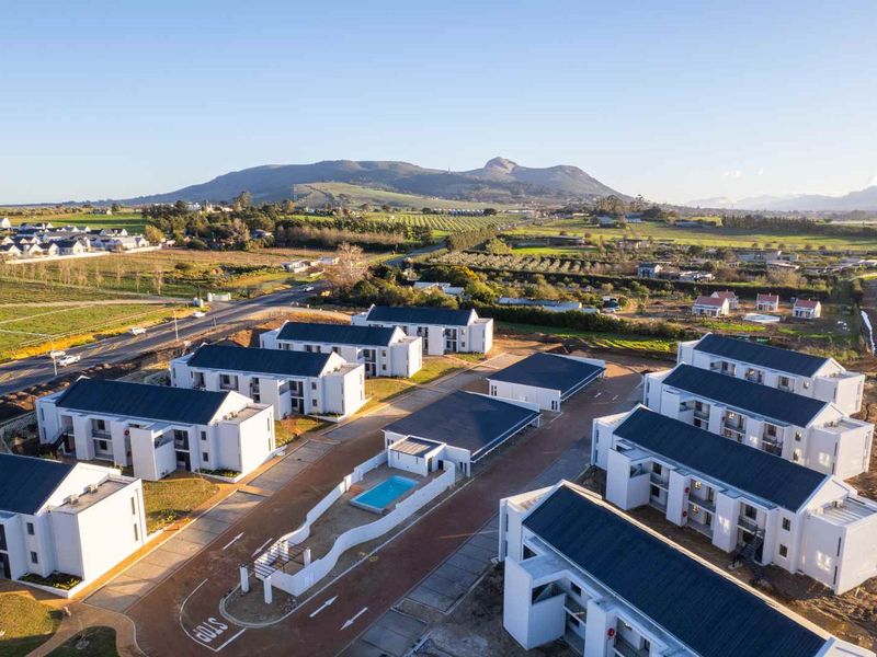 Aerial view of a modern residential apartment complex featuring multiple buildings, a communal swimming pool, and paved access roads in a scenic landscape.