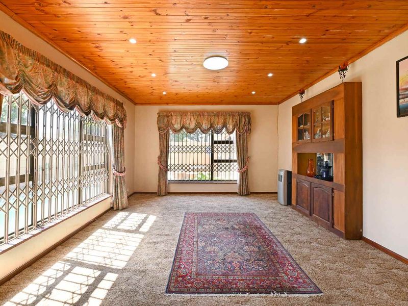 Spacious living room featuring a warm timber-paneled ceiling, recessed lighting, built-in wooden cabinetry, and large windows secured with metal security gates.