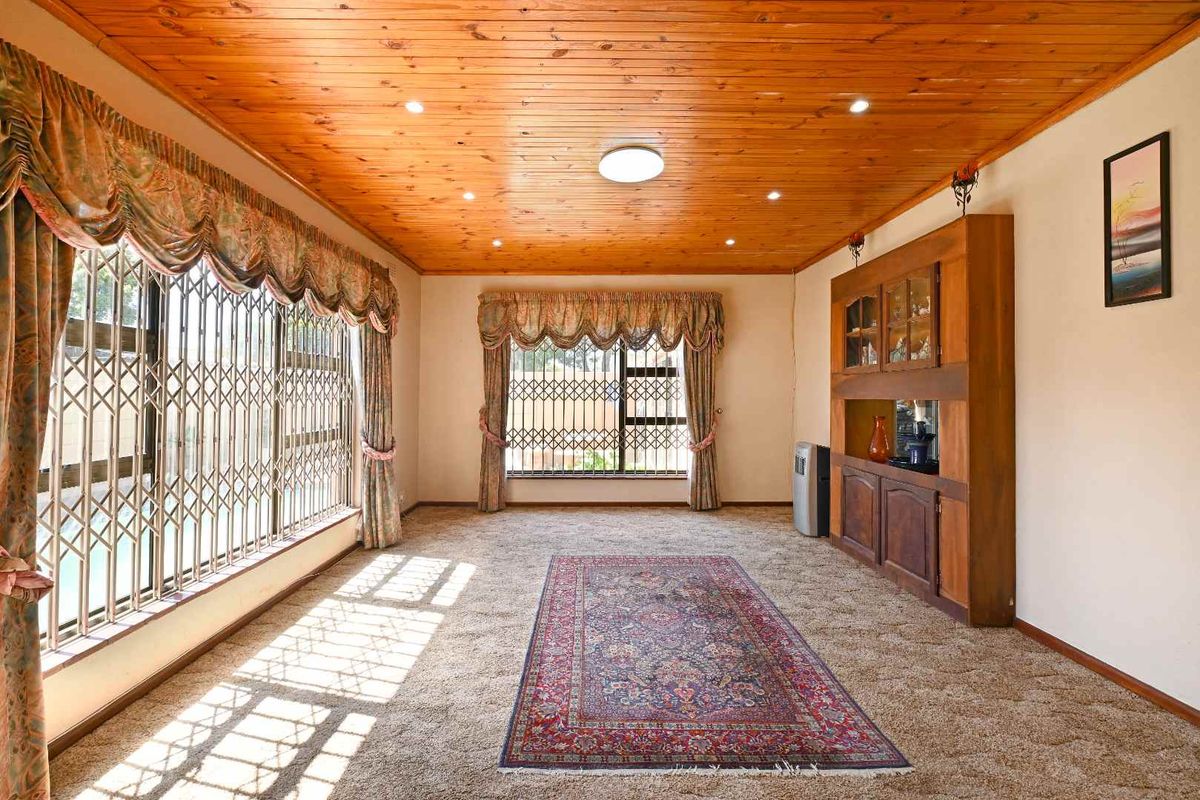 Spacious living room featuring a warm timber-paneled ceiling, recessed lighting, built-in wooden cabinetry, and large windows secured with metal security gates.
