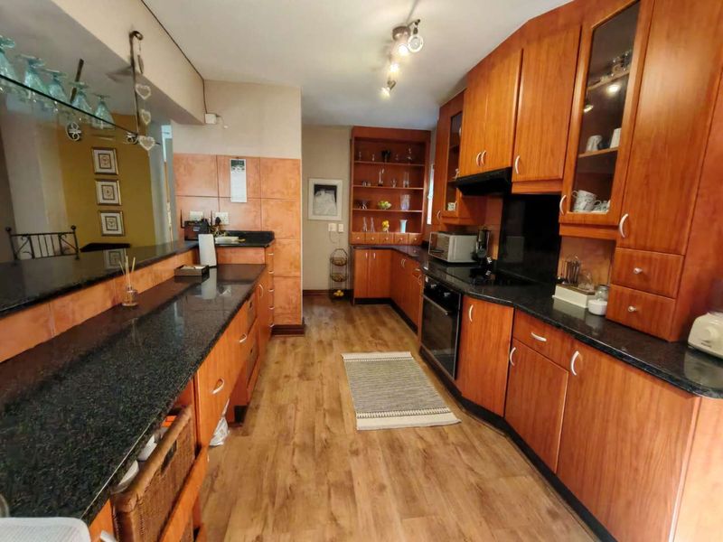 A functional kitchen featuring extensive wooden cabinetry, dark granite countertops, built-in cooking appliances, and durable laminate flooring.