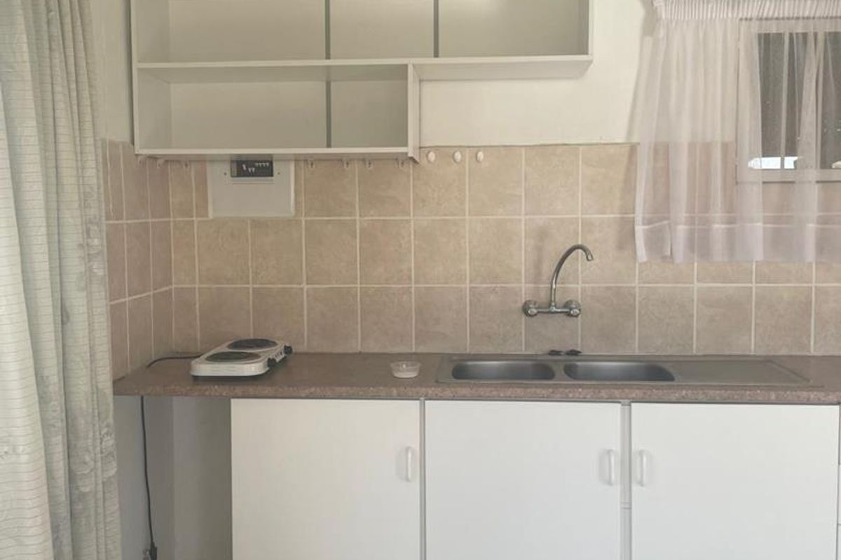 A functional kitchen area featuring white cabinetry, a double stainless steel sink, tiled splashback, and tiled flooring.